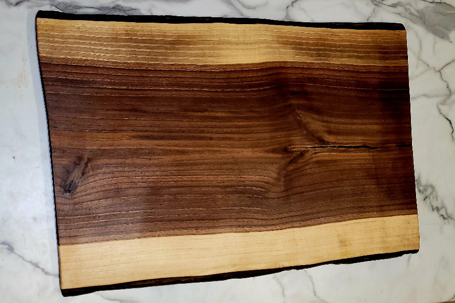 A short black walnut grazing board with a dark interior, light strip on the sides and black bark.