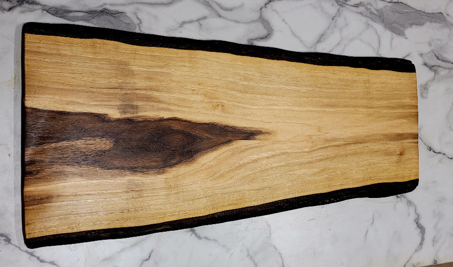 A Black walnut Grazing board with a light colour, some dark colouring at one end, and black bark on exterior