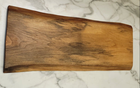 A live edge black walnut grazing board with basically a light background and attractive grain formations through the surface of the board