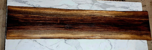 Extra long black walnut grazing board with light, medium, and dark streaks from the natural wood grain. Beautiful natural pattern creating an overall striking appearance with live wood edges. The grazing board is pictured on top of a granite table in the woodshop. 